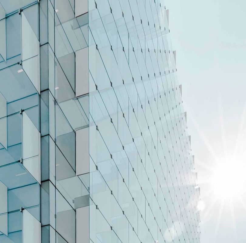 Immeuble moderne en verre reflétant la lumière du soleil, symbole de propreté et d’expertise technique de HYGEA SERVICES